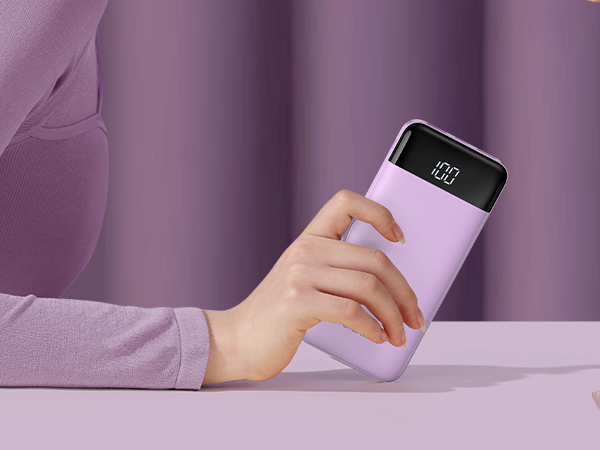 Lavender-colored portable power bank with digital display. Hand holding device showcases its compact size and smooth texture.