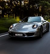 Silver-gray luxury sports car photographed at night with illuminated background, displaying sleek aerodynamic design and distinctive grille.
