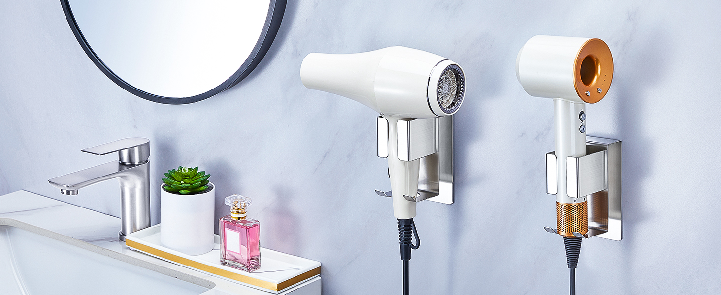 Wall-mounted hair dryer holders in white and copper finishes, shown installed on bathroom wall alongside decorative shelf with pink accessories and small plant.