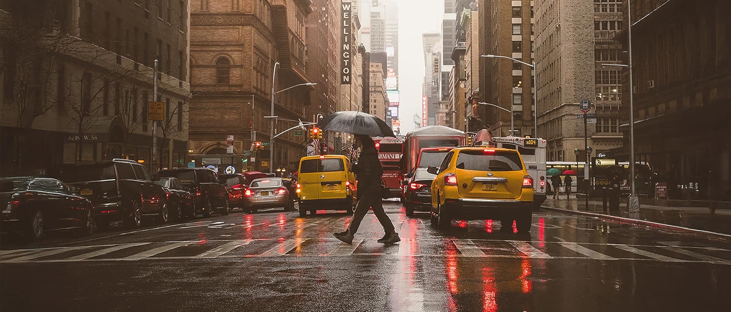 City street, with rain and person walking with umbrella across street
