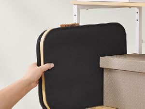 Black rectangular storage or organizing unit with gold or brass accent trim being assembled or installed.