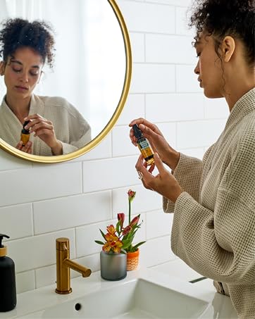 Person wearing a robe in a bathroom holding Herb Pharm&amp;amp;#39;s soothing throat spray.