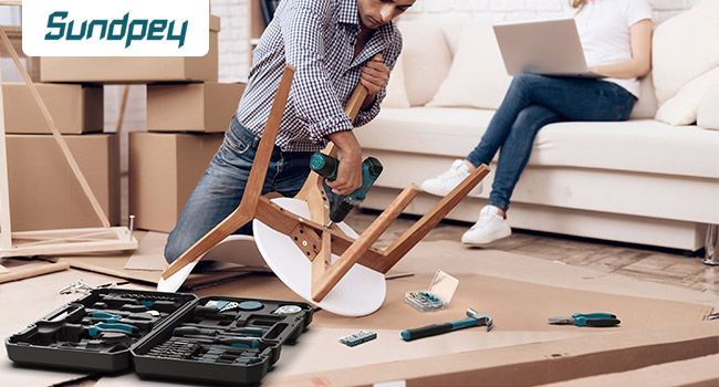 Assembly or furniture tools spread on floor with toolbox open, showing various hand tools and parts near cardboard boxes and sofa.