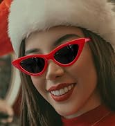 Woman in red sweater and Santa hat wearing sunglasses, smiling outdoors with Christmas decorations in background.