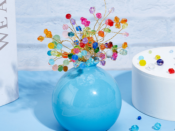 Light blue ceramic vase containing colorful beaded floral arrangement with bright pink, orange, and multicolored crystal stems.