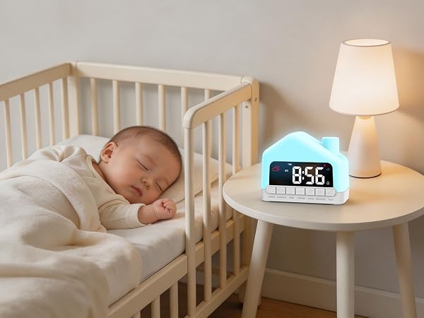 Sleeping infant in white bedding inside wooden crib next to white nightstand with digital clock displaying "8:56" and white table lamp with warm lighting.