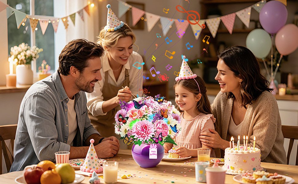 Indoor party or celebration setting with three people gathered around a table with colorful decorations, balloons, flowers, and wrapped presents. Festive bunting and warm lighting visible.
