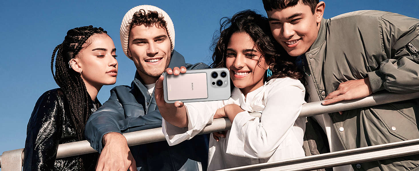 Smartphone with multiple camera lenses being used to take a group selfie outdoors. Device has a light-colored body and is held horizontally.