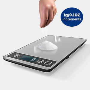 Digital kitchen scale with flat stainless steel surface and touch controls. Display shows 0g. Hand sprinkling white powder. Blue circle indicates 1g/0.1oz increments.