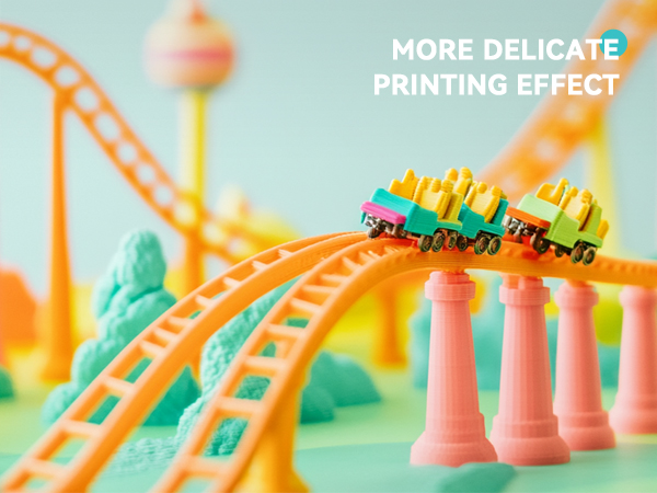 Miniature roller coaster model with pastel-colored tracks and tiny train cars. Features curving orange rails supported by pink pillars against a soft-focus background.