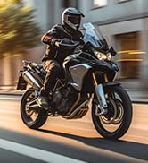 Motorcycle rider in motion on urban street, wearing black protective gear and helmet, riding dark-colored sport bike with gold accents.
