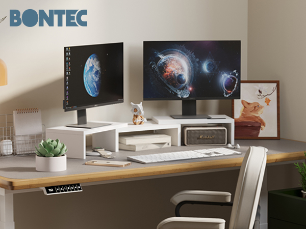 Dual monitor desk setup with space-themed wallpapers, white monitor riser, keyboard, and office accessories on a wooden desk with a chair.