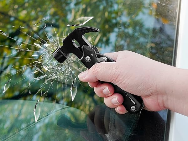 Hand holding a black emergency hammer tool breaking car window glass, demonstrating its use for vehicle escape or rescue.