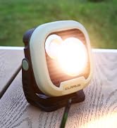 Portable LED light with white housing shown illuminated outdoors on wooden surface, featuring bright white light output.