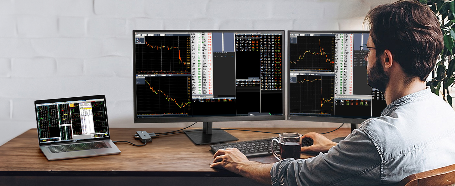Trading or analysis workspace setup with multiple monitors displaying financial charts and graphs, alongside a laptop on wooden desk.