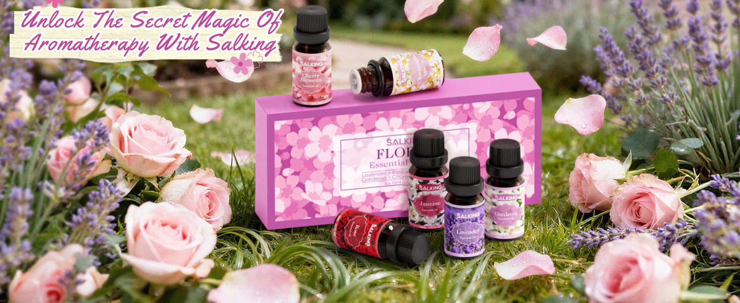 Collection of essential oil bottles arranged among pink roses and floral elements on grass, creating a natural product photography setup.