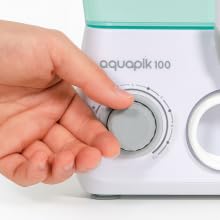 Text reads 'aquoptik 100'. Close-up of a hand turning a white control dial on a device with minimalist design featuring circular controls.