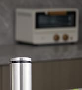 Stainless steel cylindrical container or vessel with brushed metal finish, shown in partial view against blurred background.