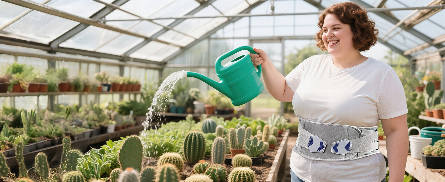 Green plastic watering can in use, watering various cacti and succulent plants in a greenhouse setting. Rows of potted plants visible on shelves.