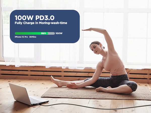 Laptop displaying '100W PD3.0' charging indicator with progress bar, shown on wooden floor with exercise mat.