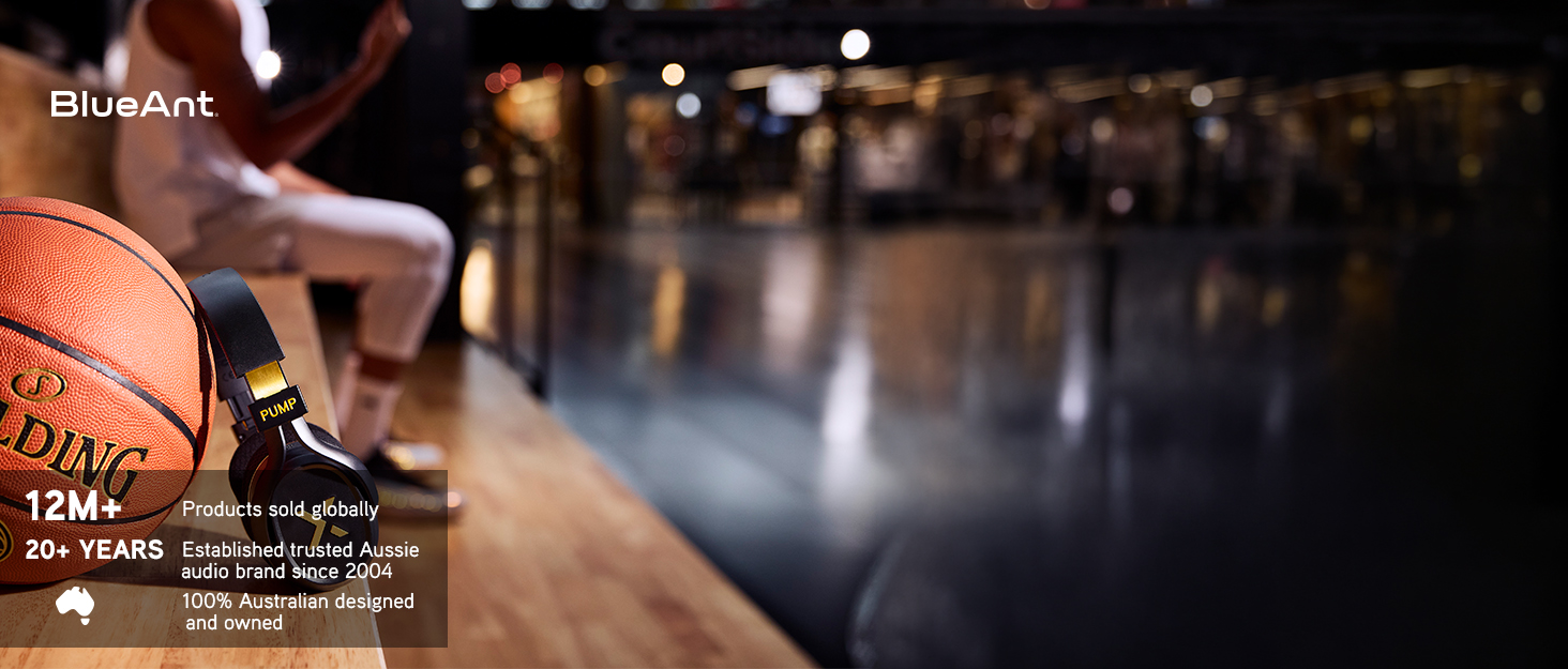 BlueAnt Pump X in Black &amp; Gold leaning against a basketball in a basketball arena