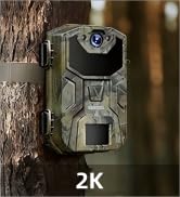 Green camouflage-patterned outdoor camera mounted on tree trunk. Features large lens, infrared sensors, and '2K' text indicating high-resolution capability.