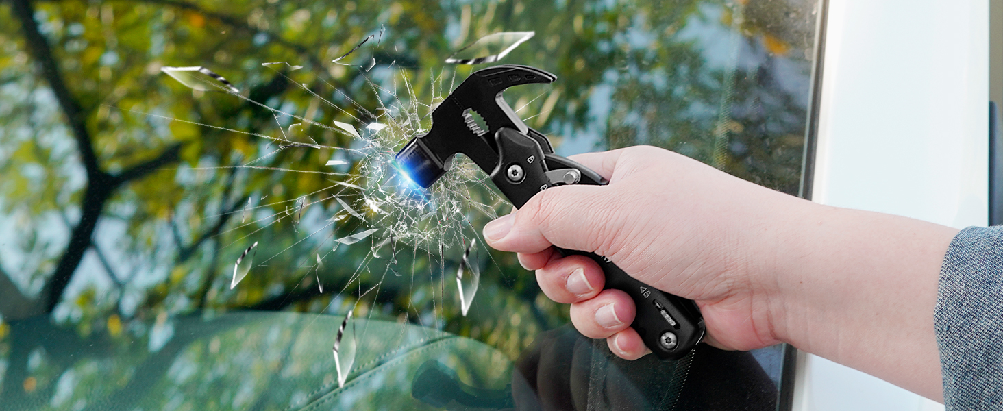 Hand holding emergency car tool with hammer head, shown breaking glass in demonstration of safety feature.