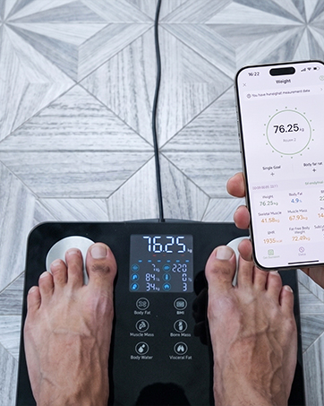 The body fat scale is placed on the floor, and a mobile phone shows the FeelFit app interface.