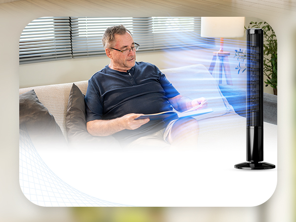 Man sitting on couch reading with fan blowing around the room