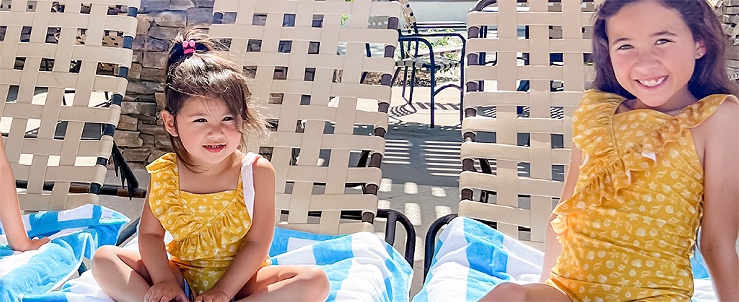 Little girls in summer clothes, smiling while sitting on beach towels
