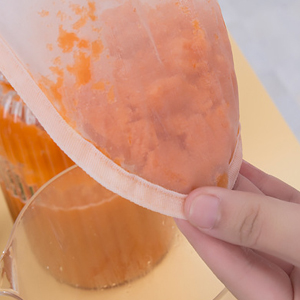 a hand is pouring a bag of carrot juice into a measuring cup.