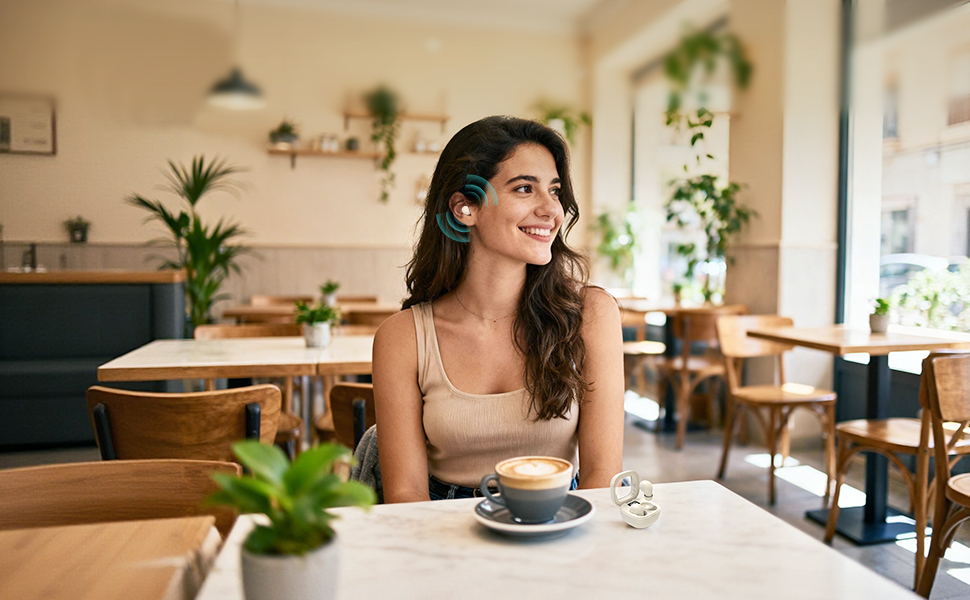 Woman wearing mini earbuds in a cafe. Shows the discreet, low-profile fit for work or office.