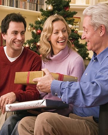 Group seated on couch during holiday season, sharing gifts and expressing joy, with decorated Christmas tree visible in background.