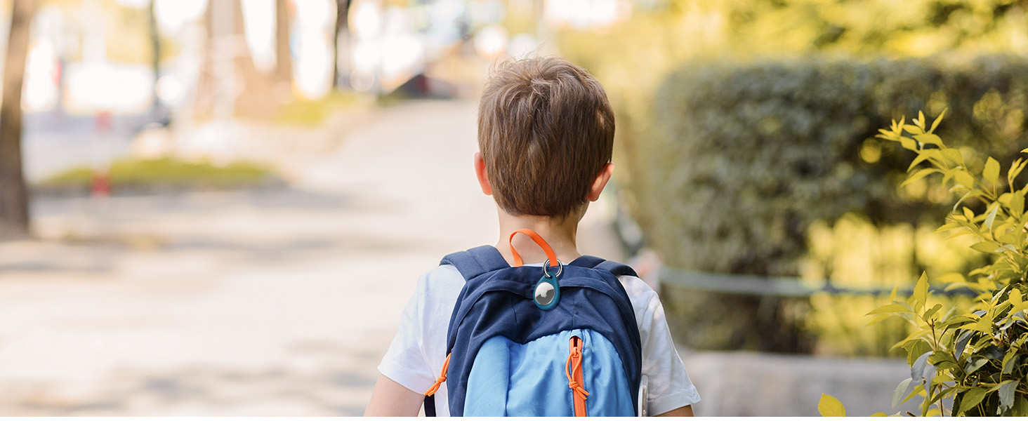 Child wearing a blue backpack walking on a path lined with green bushes.