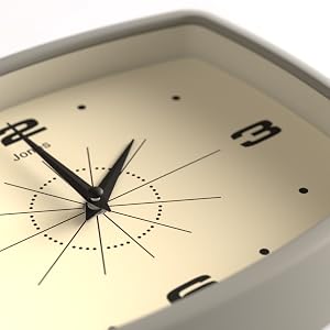 Close-up of a square analog wall clock with a champagne-colored face. Black hands point to 10:10. Minimalist design features dot markers and thin lines for hours.