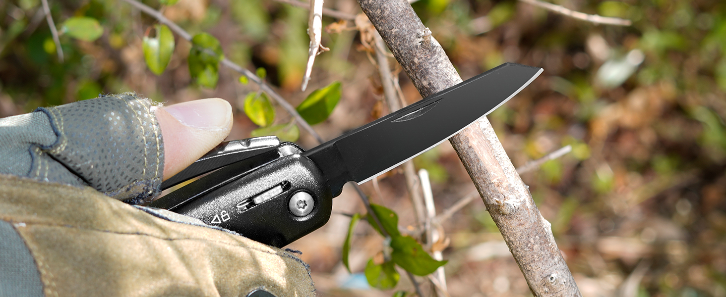 Black folding pocket knife with textured handle grip being used to cut a small branch outdoors.