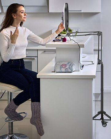 Woman using a countertop-mounted articulating arm to hold a tablet or screen above a kitchen workspace, demonstrating hands-free device use while cooking.