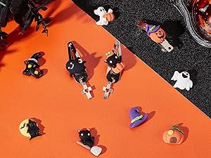 Assortment of miniature Halloween-themed decorations on orange and black surfaces. Includes pumpkins, ghosts, witches, and spider figurines.