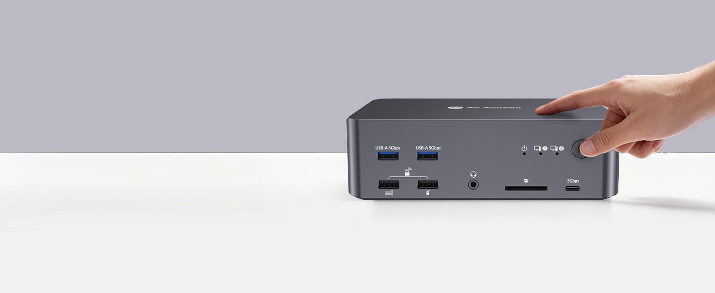 Gray electronic device or hub shown from side angle with multiple ports visible. Hand reaching to interact with top surface controls.