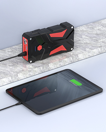Black and red portable power bank with rugged angular design charging a tablet device on marble surface.