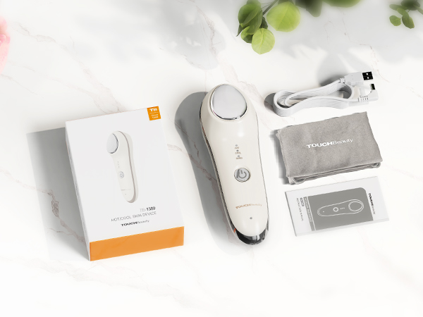 White handheld electronic device with oval shape and button, displayed with packaging box, charging cable, and instruction manual on light background with plant leaves.