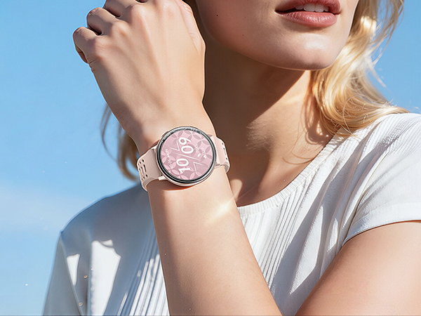 Close-up of a rose gold smartwatch with pink digital display worn on wrist against light blue sky background.