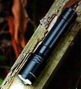 Close-up shot of a black tactical flashlight mounted on wooden surface, showing metallic construction and compact design.