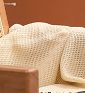 Partial view of a beige or cream-colored textured fabric, possibly part of a sofa or chair cushion.