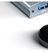 Partial view of a rectangular electronic device with a metallic finish, possibly a portable charger or external hard drive.