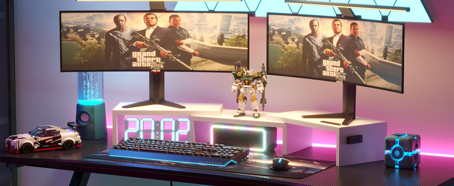 Gaming setup with dual monitors, RGB keyboard, illuminated mouse pad, and colorful ambient lighting. Decorative figurines and toy cars visible.