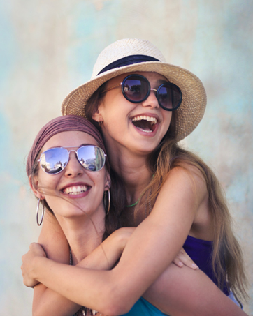 Two laughing women in casual outfits on blue-beige background.