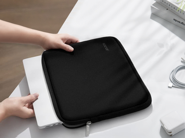 Black laptop sleeve case with zipper being opened to insert a white laptop. Charger and cable visible on table.