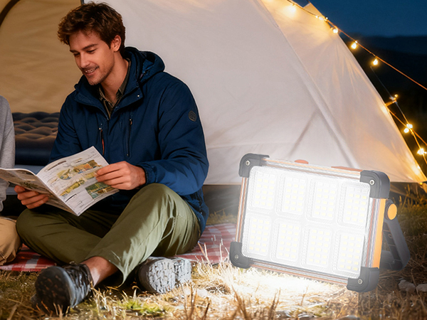 Camper reading book inside tent at night with portable LED work light as camping lantern