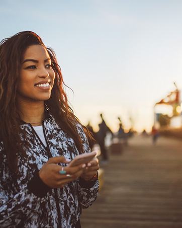 Lifestyle image of a woman on a pier holding a phone